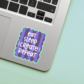 Laptop with a 'eat sleep create repeat' sticker on a light green background