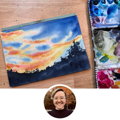 Painting of a sunset with watercolor techniques on a wooden surface, next to an open watercolor set.